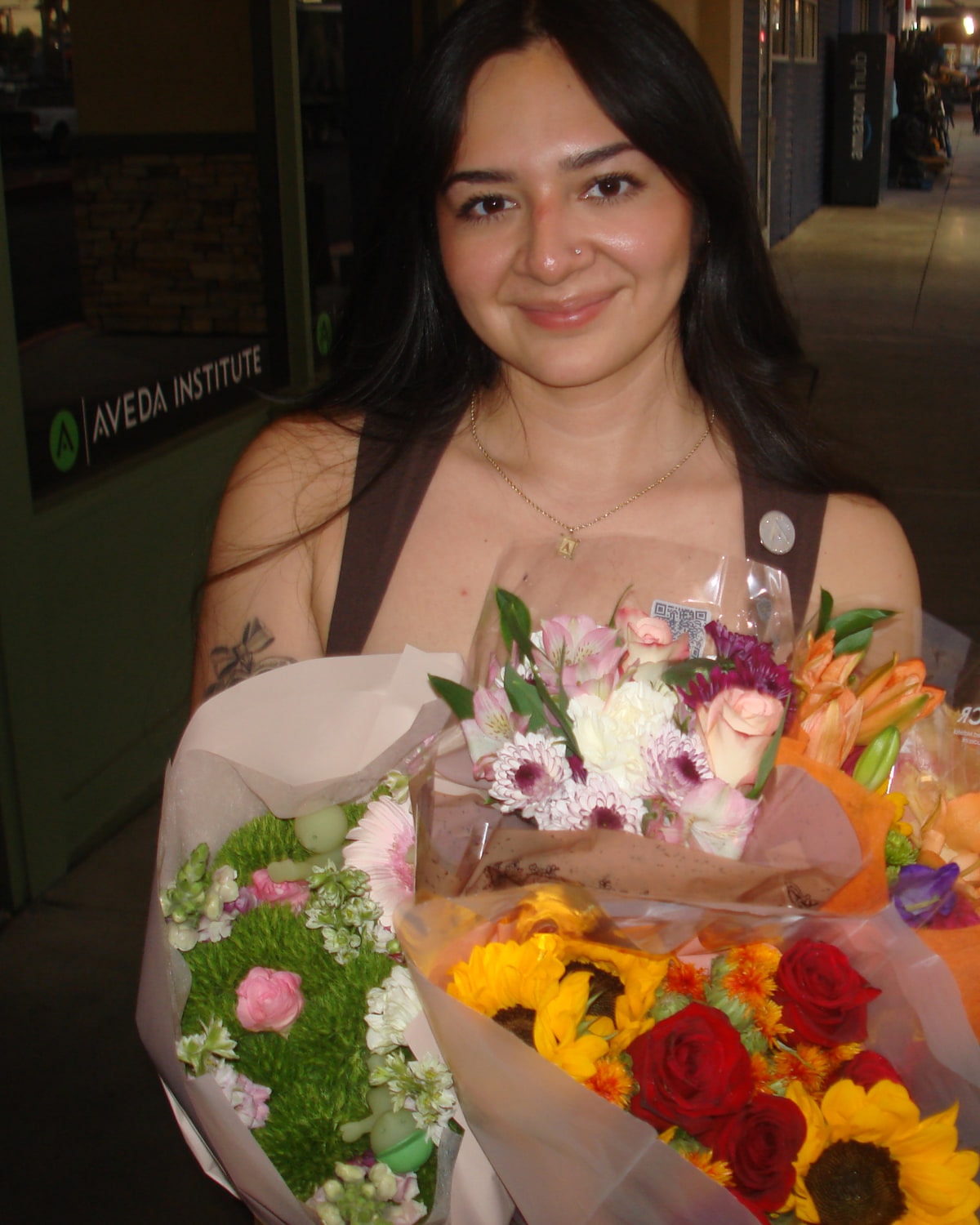 Arianna outside the Aveda Institute on graduation day, holding bouquets of flowers